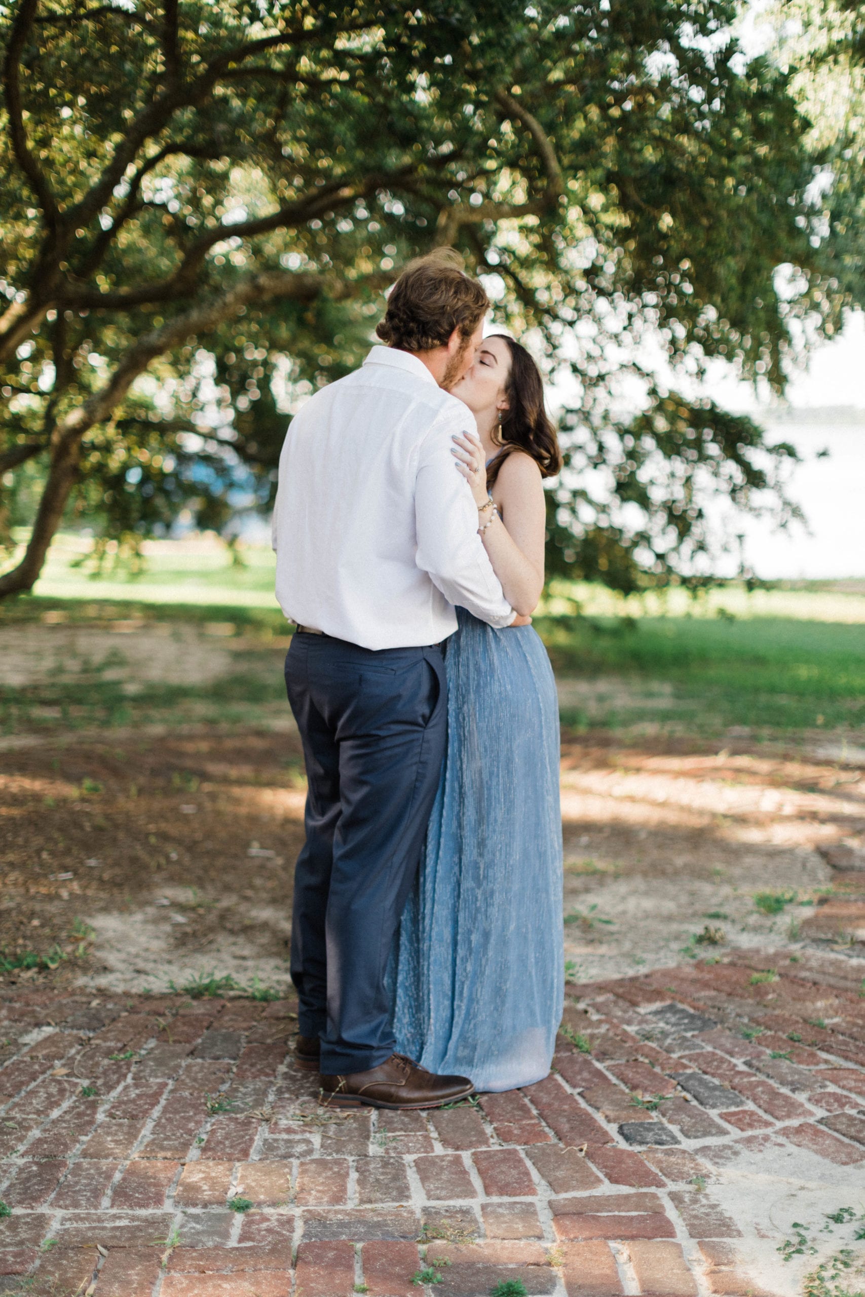 engaged couple embrace and kiss under oak tree at Biloxi's Old Brick House
