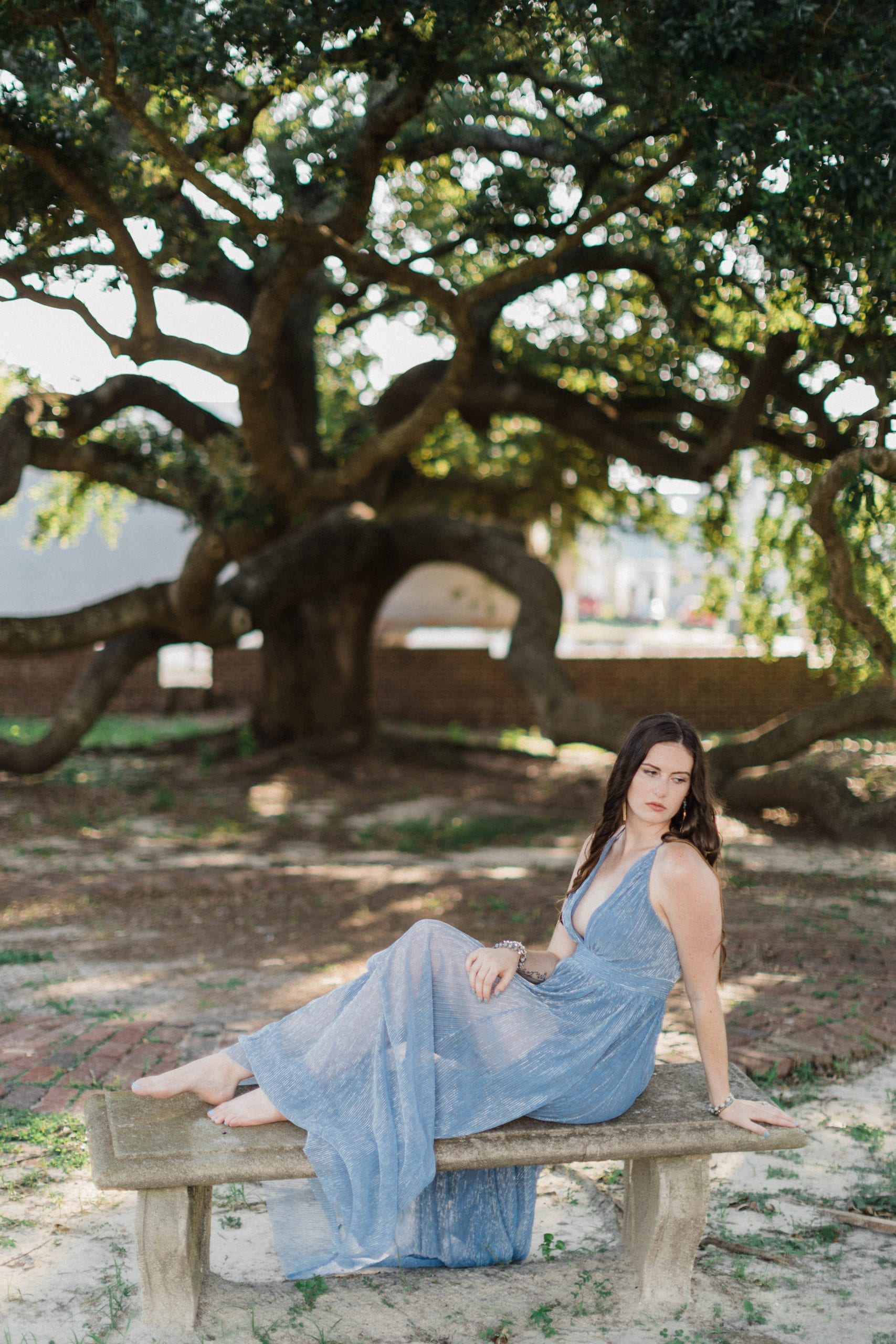 portrait of soon to be bride, sitting on cement bench under mossy oaks