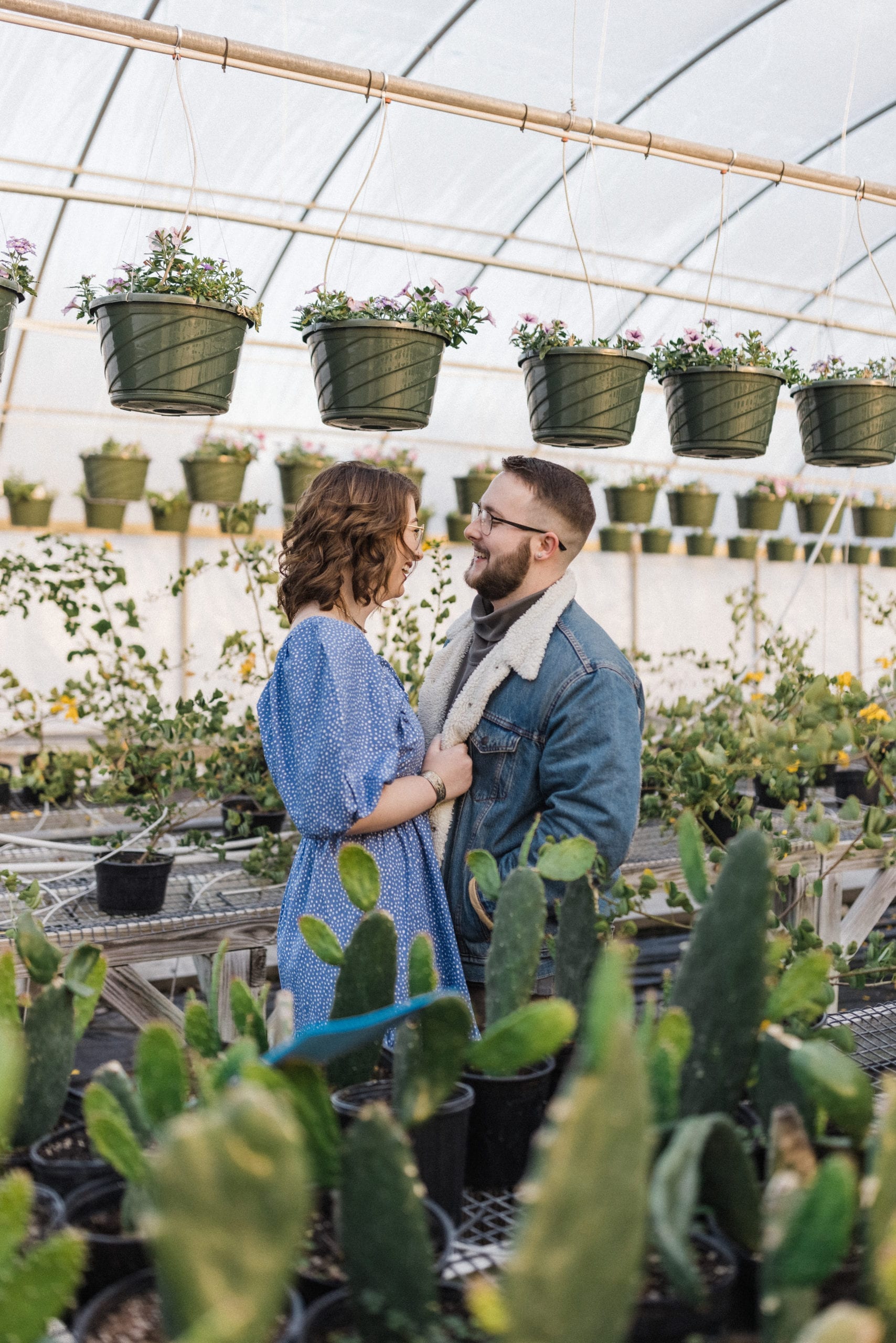 engaged couple stand in greenhouse laughing