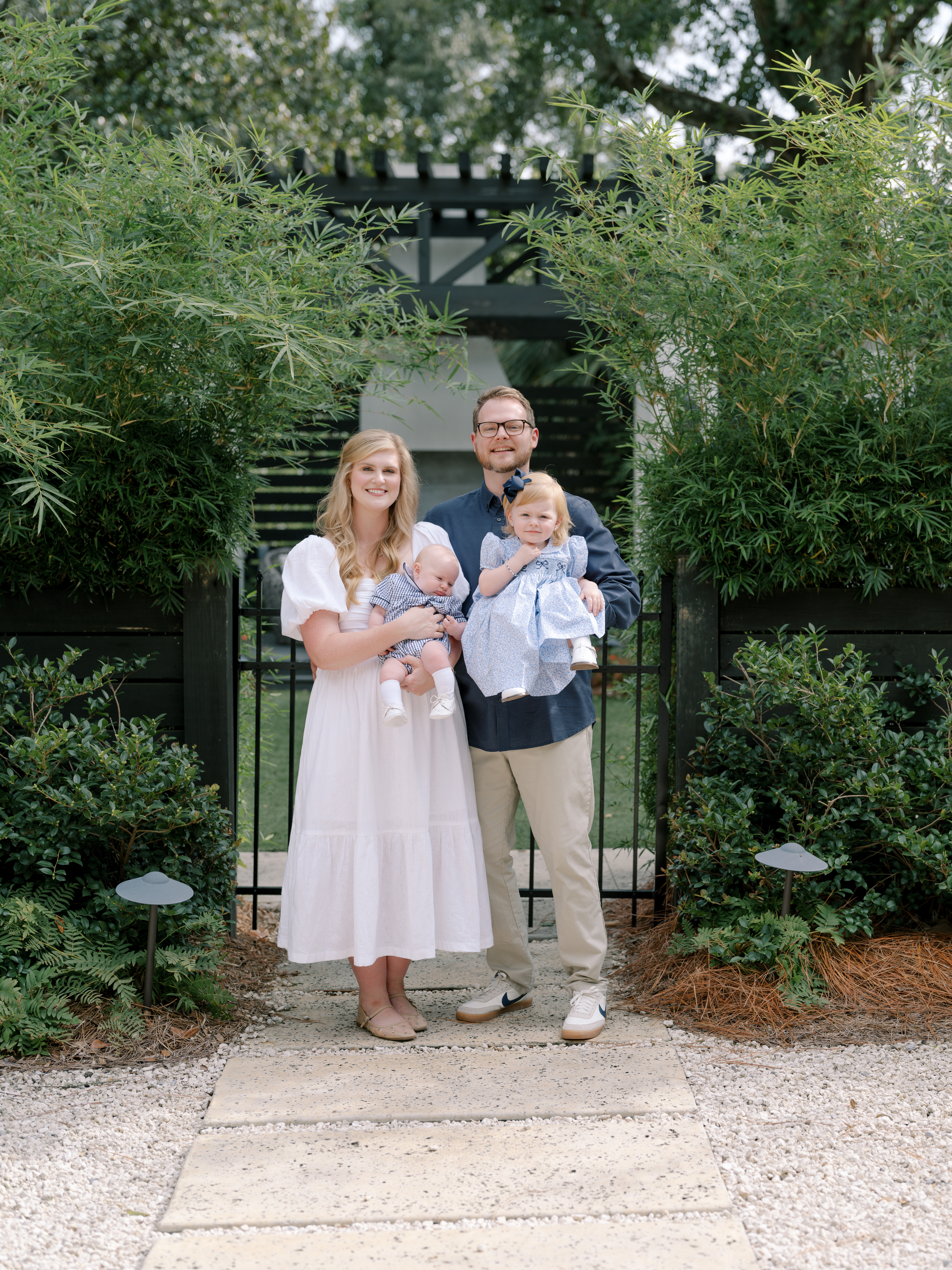 Mom, dad, and two young children pose before gate and greenery.